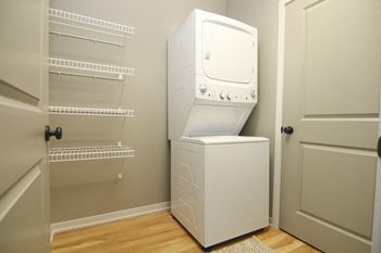 Stacked washer and dryer combo with shelving for storage in laundry room at The Villas at Wilderness Ridge in South Lincoln, Nebraska